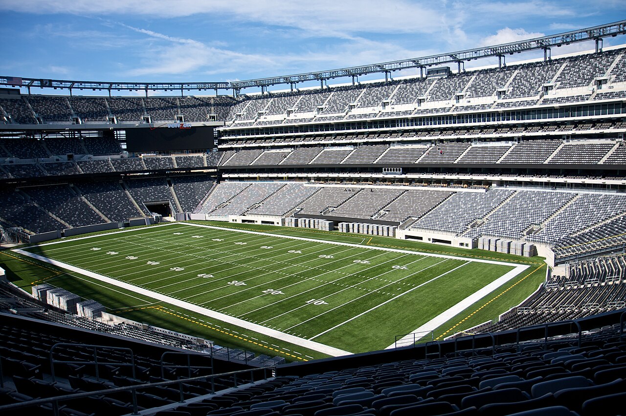 The interior of MetLife Stadium, an empty bowl with tiers of grey seats and a green field.